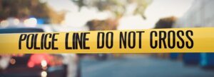 A close-up of a yellow "Police Line Do Not Cross" tape highlights concerns over church security, with blurry background features like police car lights and trees accentuating the gravity of the scene.