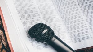 A black microphone rests on an open book with text, evoking themes of communication and presentation. This scene blends the realms of literature and audio with a hint of theology, focusing on both the textual content and the microphone, echoing elements of church technical arts.