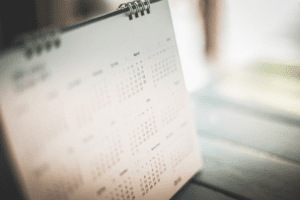 A close-up of a spiral-bound calendar open on a wooden table, highlighting the months of March and July. The scene captures productivity as it unfolds in soft, natural light, with blurred surroundings adding to the focus.