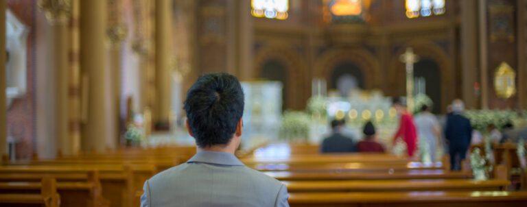 A person in a gray suit sits in a church pew, facing the altar. The ornate interior suggests it's welcoming to first-time visitors, with blurred figures in the background near the altar, possibly during a ceremony or service aimed at building visitor retention.