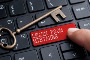 An antique key rests on a keyboard, with a red key labeled "LEARN FROM MISTAKES." A finger points to it, symbolizing the wisdom gained from church management mistakes.