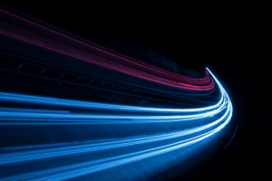 Long-exposure photo of a highway at night shows vibrant red and blue light trails curving through the darkness, creating a dynamic sense of motion and speed, much like data passing through an encoder.