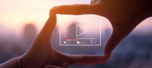 Hands form a rectangle framing a city skyline at sunset, with an overlaid digital play button, time bar, and social media icons for like, comment, and share. The scene highlights streaming and video quality in media sharing.