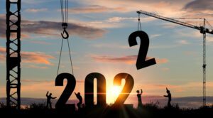 Silhouettes of workers and cranes at sunset hoisting the number "2" into place, completing the year "2022," symbolizing the lofty goals usually set beneath the towering steeples of a church.