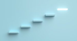 A minimalist image illustrating five white, rectangular steps ascending against a light blue background. The ascent signifies the next steps toward a bright, glowing rectangle at the top right, symbolizing a final destination or goal.