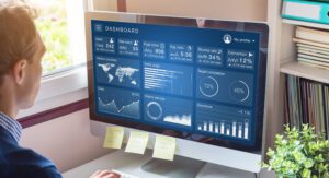 A data enthusiast is intently examining a computer monitor that displays a detailed analytics dashboard. The screen showcases charts, graphs, and statistics on user data, page views, and conversions. Sticky notes are thoughtfully attached to the bottom of the monitor.