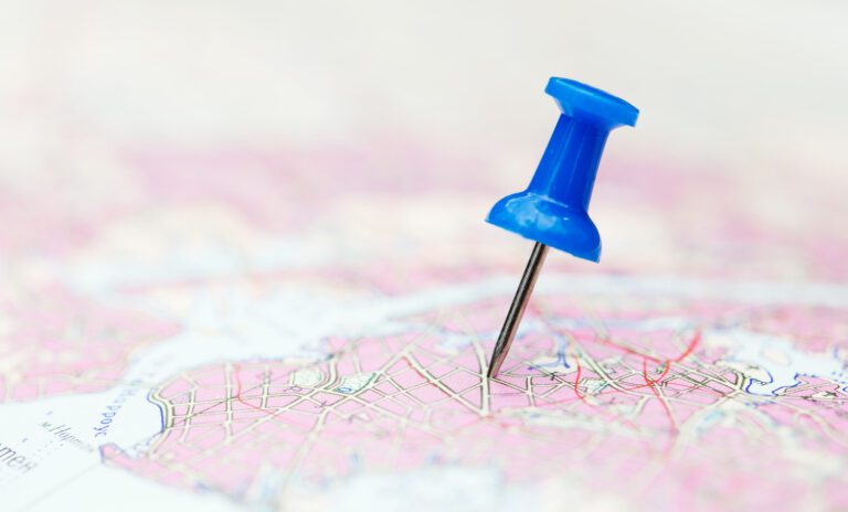 A blue pushpin is inserted into a colorful map on the website, marking a specific location. The map showcases a network of roads in various shades of pink and white, with blue areas indicating bodies of water—a helpful tool to plan your visit efficiently.