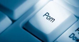 Close-up of a computer keyboard with a key labeled "Porn." Styled with a blue tint, it stands out prominently as if it were an unspoken secret against the blurred backdrop—a contrast akin to whispers in a church.