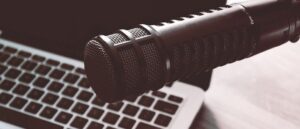 A close-up of a microphone takes center stage, perfectly poised for your own podcast journey. In front of a slightly blurred laptop keyboard, this setup captures the first steps towards creating compelling audio content.