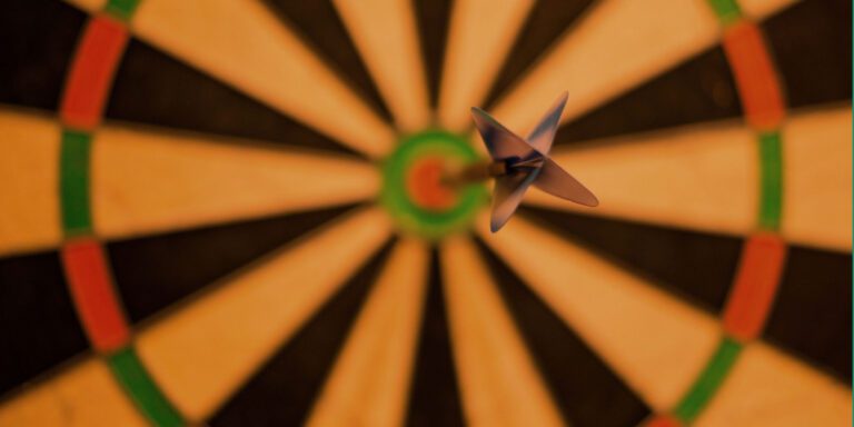Close-up view of a dart in mid-air, expertly aimed, about to hit a dartboard centered perfectly on the bullseye. Like finely tuned church goals, it’s guided with precision through traditional black, white, and green sections.
