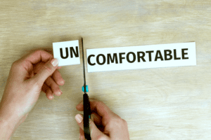 A pair of hands is using scissors to cut the word "UNCOMFORTABLE" into two pieces, symbolizing how important discussions can separate "UN" from "COMFORTABLE." This visual suggests that addressing uncomfortable issues, much like those the Church needs to talk about, starts by breaking them down.