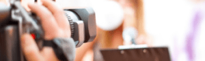 Close-up of a video camera focused on a presenter holding a microphone and clipboard in a blurry background, seamlessly integrating the elements needed for an engaging recording session. Capture this moment as it can offer invaluable SEO benefits, enhancing visibility for countless reasons.