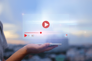A hand holds a smartphone, projecting a transparent video player interface with a play button, progress bar at 1:03 of 2:56, and control buttons. Against a blurred cityscape, the scene invites you to stream viral content effortlessly and share the moment.