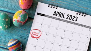 A calendar page for April 2023 is shown, with "Easter Sunday" marked on April 9th. Beside it, four colorful Easter eggs rest on the turquoise wooden surface, ready to celebrate by ushering in a joyful church gathering.