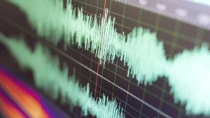 A close-up of an audio waveform displayed on a computer screen during streaming video audio. The green waveform stands out against a dark background with grid lines, intersected by a vertical red line, likely marking a specific point in the track.