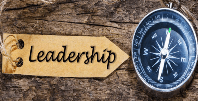 A compass points north beside a wooden tag with "Leadership" etched on it. Resting on a textured wooden surface, the scene evokes a sense of direction and guidance, much like church leaders offer to their congregation.