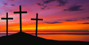 Three crosses silhouetted against a vibrant sunset sky with hues of orange, pink, and purple create the perfect backdrop for a successful Easter service. Positioned on a hill overlooking a calm body of water, the scene invites contemplation and serenity amidst the event's sacred ambiance.