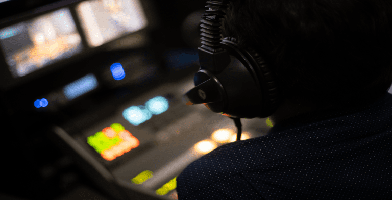 A person wearing headphones sits at a control panel with colorful buttons and screens, fully focused on their task in the dimly lit studio. The impact of their work is akin to orchestrating a seamless paid streaming service, ensuring everything runs smoothly.